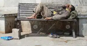 pobre mendigo sin hogar o refugiado durmiendo en un sucio banco de madera una calle la ciudad durante el dia social concepto e x